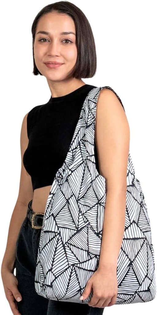 Woman carrying the Nanobag ultralight foldable reusable tote bag with black and white geometric pattern, demonstrating its full-size 19-liter capacity for travel, shopping, and everyday carry.